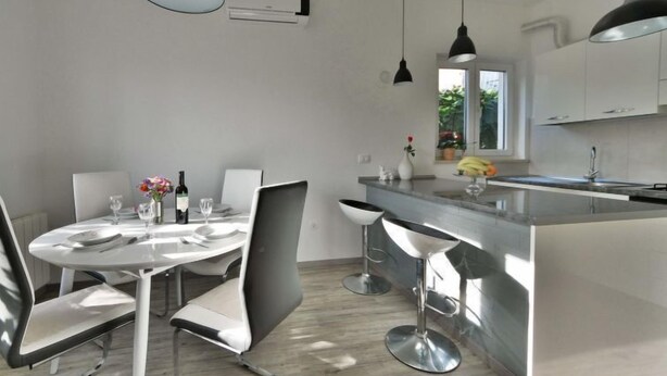 A modern kitchen with a dining area, featuring a central island, pendant lighting, and a window with a view of greenery. - Apartment Karlo by Interhome (Opatija/Rukavac)