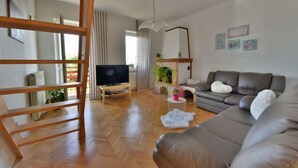 A modern living room with a wooden floor, a grey sofa, a television on a stand, a fireplace, and a ceiling fan. - Apartment Karlo by Interhome (Opatija/Rukavac)