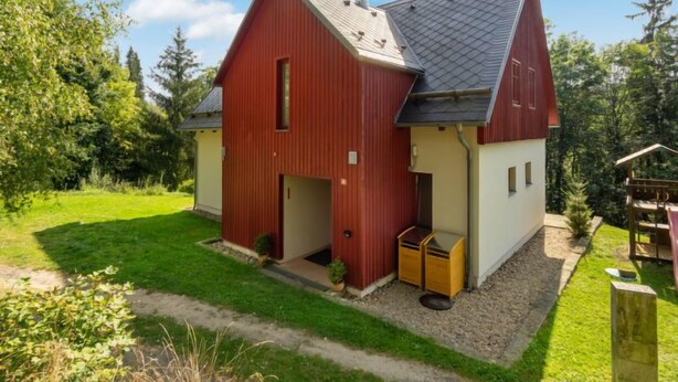 Une maison de style grange, peinte en rouge, avec un toit en pente, un porche à l’avant et un petit garage attenant.