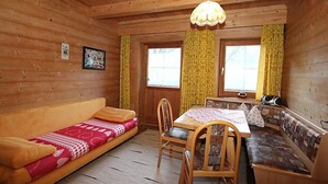 Ein gemütliches Blockhaushaus-Interieur mit Holzbalkendecke, einer Couch, einem Esstisch mit Stühlen und einer Bank.