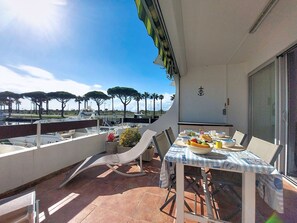 Un balcon avec une table dressée pour le dîner, des chaises, une petite plante et une vue sur la mer et les palmiers.