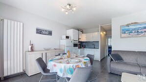 Eine moderne Küche mit weißen Schränken, ein Essbereich mit rundem Tisch und ein graues Sofa.