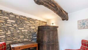 Een rustiek interieur met een stenen muur, een houten vat, een houten tafel en geruite stoelen.