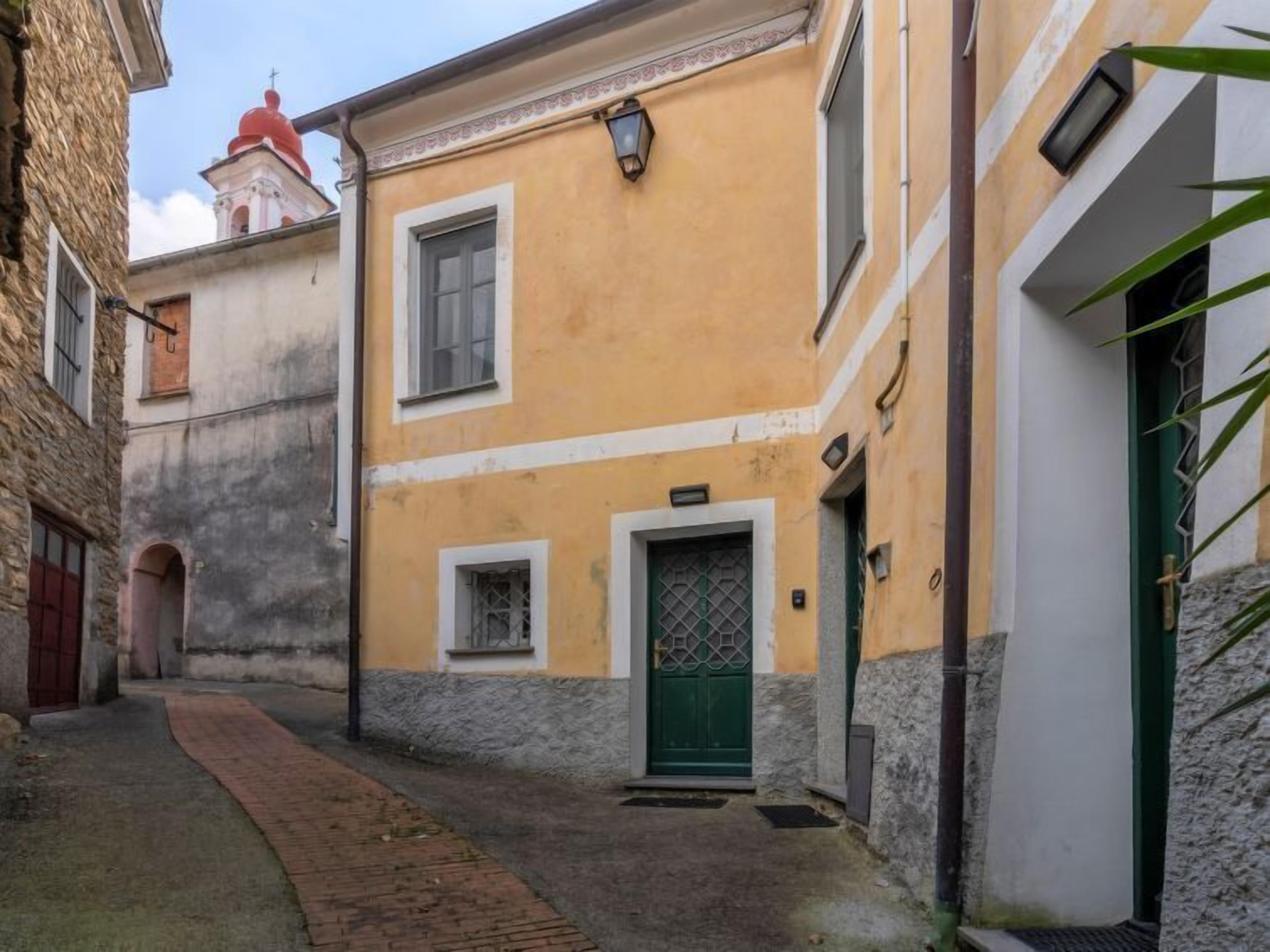 A narrow alleyway with a yellow building featuring a green door and a small window.