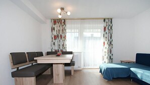 A modern room with a wooden dining table, benches, a blue sofa, and a window with patterned curtains. - Alpenrose by Interhome (See)