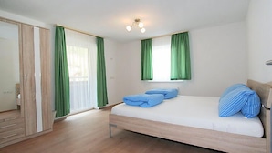 A bedroom with a wooden bed, green curtains, and a ceiling light fixture. - Alpenrose by Interhome (See)