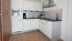 A compact kitchen with white cabinets, a built-in oven, a coffee maker, and a stainless steel range hood. - Alpenrose by Interhome (See)