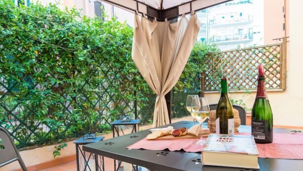A dining area with a table set for two, featuring a bottle of wine, glasses, and a book.