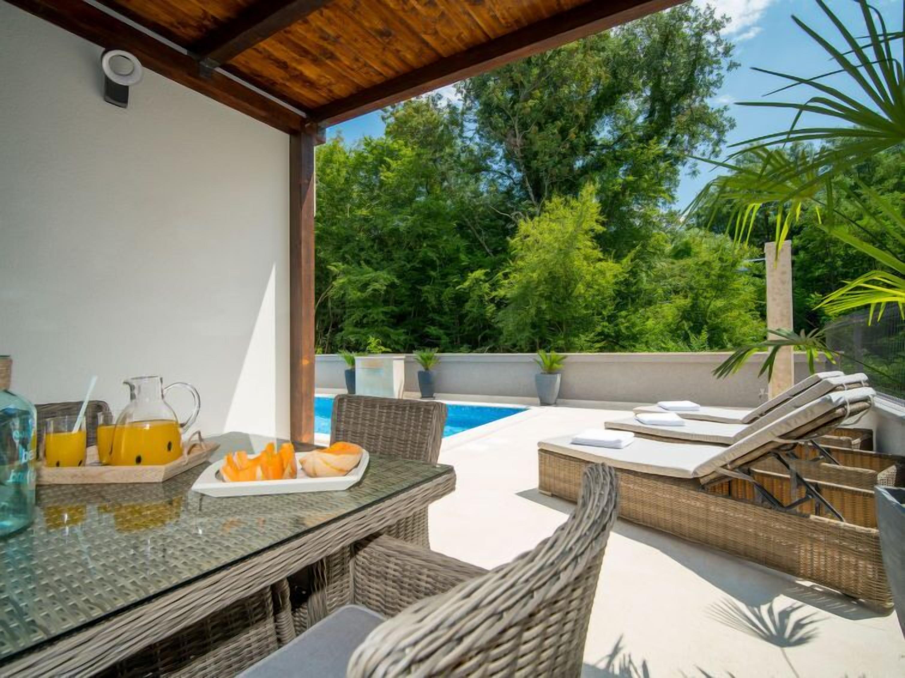 An outdoor patio with a table set for breakfast, a pool, and lounge chairs.