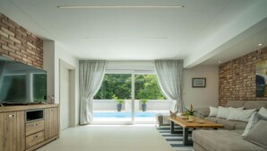 A modern living room with a TV on a wooden cabinet, a beige sofa, a wooden coffee table, and a view of a swimming pool through large glass doors. - Vacation home Anđela by Interhome (Krk/Dobrinj)