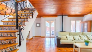 Un amplio salón con una escalera de madera, un sofá y piso de baldosas.