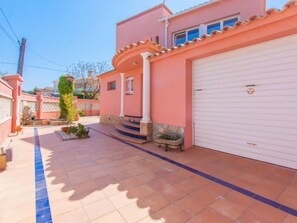 Ein zweistöckiges Haus mit weißer Garagentür, einer kleinen Veranda mit Stufen und einer gefliesten Terrasse.