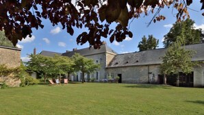 A courtyard with a grassy lawn, a stone building, and a tree with autumn leaves.