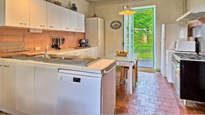 A compact kitchen with white cabinets, a built-in dishwasher, a stove, and a window overlooking a garden.