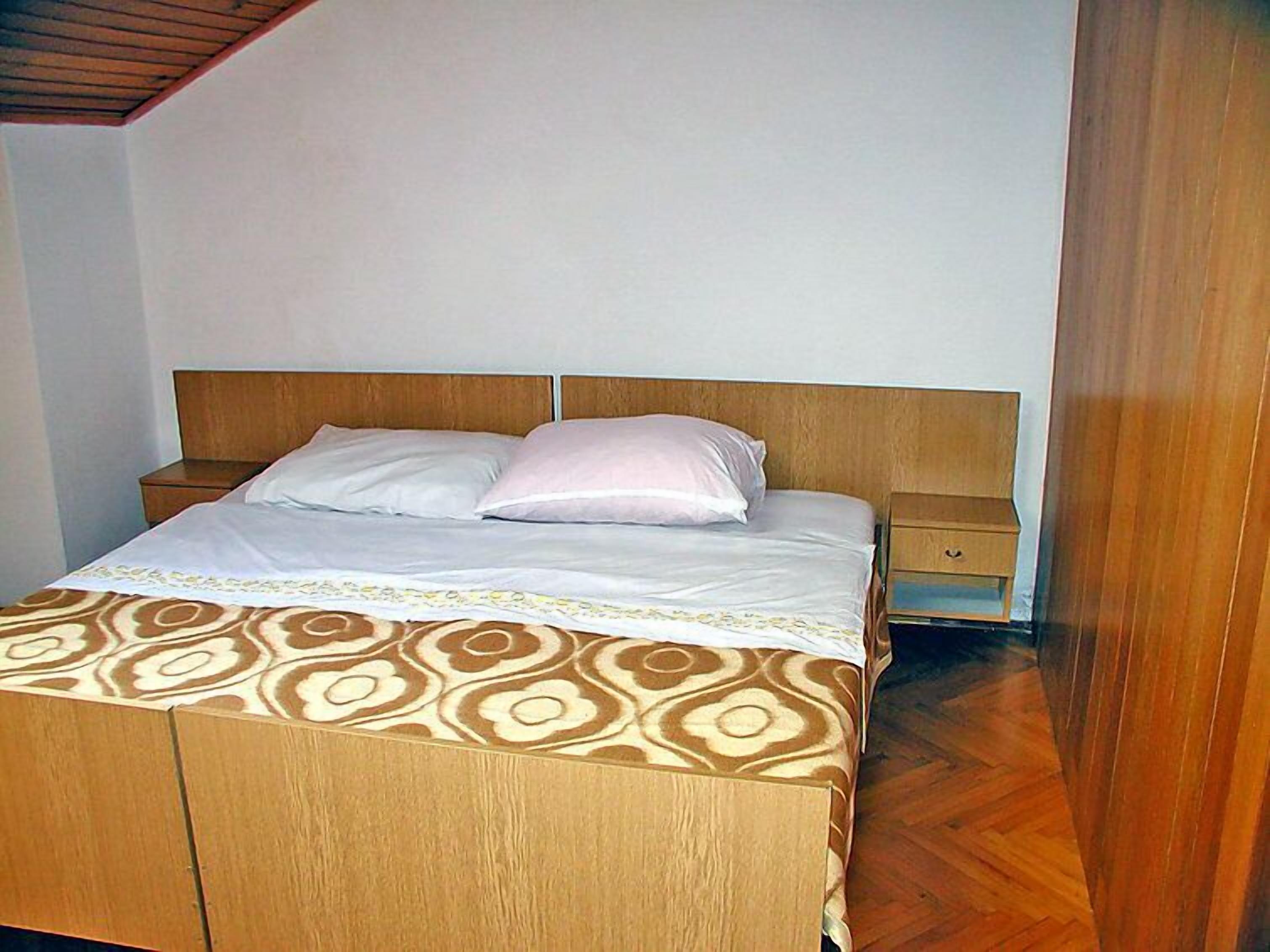 A single bed with a patterned bedspread, wooden headboard, and two bedside tables.