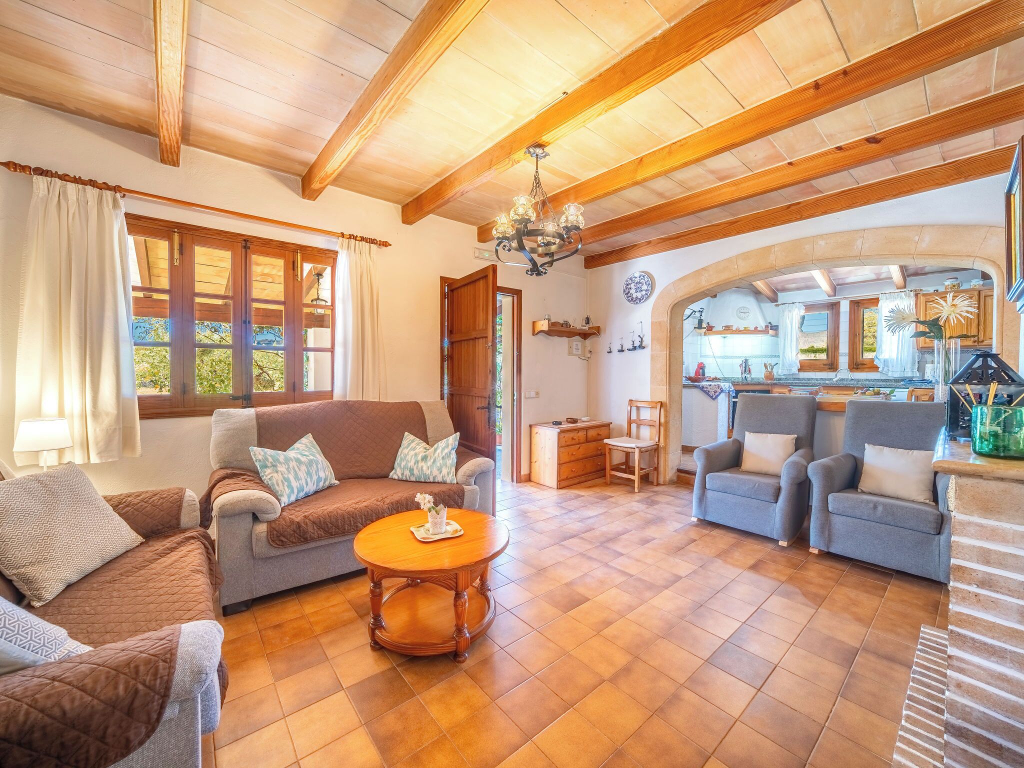 A cozy living room with a sofa, chairs, a wooden coffee table, and a kitchen visible through an archway.