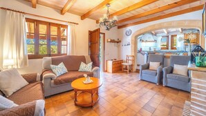 A cozy living room with a sofa, chairs, a wooden coffee table, and a kitchen visible through an archway. - Can Niu by Interhome (Pollença)