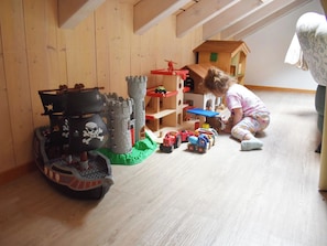 Ein Kind spielt mit Spielzeug in einem Raum mit Holzwänden und schrägverdeckter Decke.