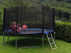 A trampoline with a safety net, set on a grassy lawn with a hedge and trees in the background.