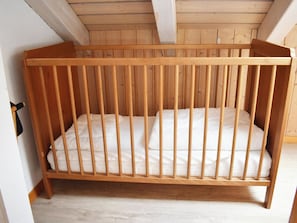 Ein hölzernes Kinderbett mit Matratze und Kissen, platziert in einem Raum mit Holzbalkendecke.