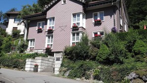 Un bâtiment à deux étages, doté d’une façade en pierre, de nombreuses fenêtres ornées de jardinières et d’un escalier menant à l’entrée.
