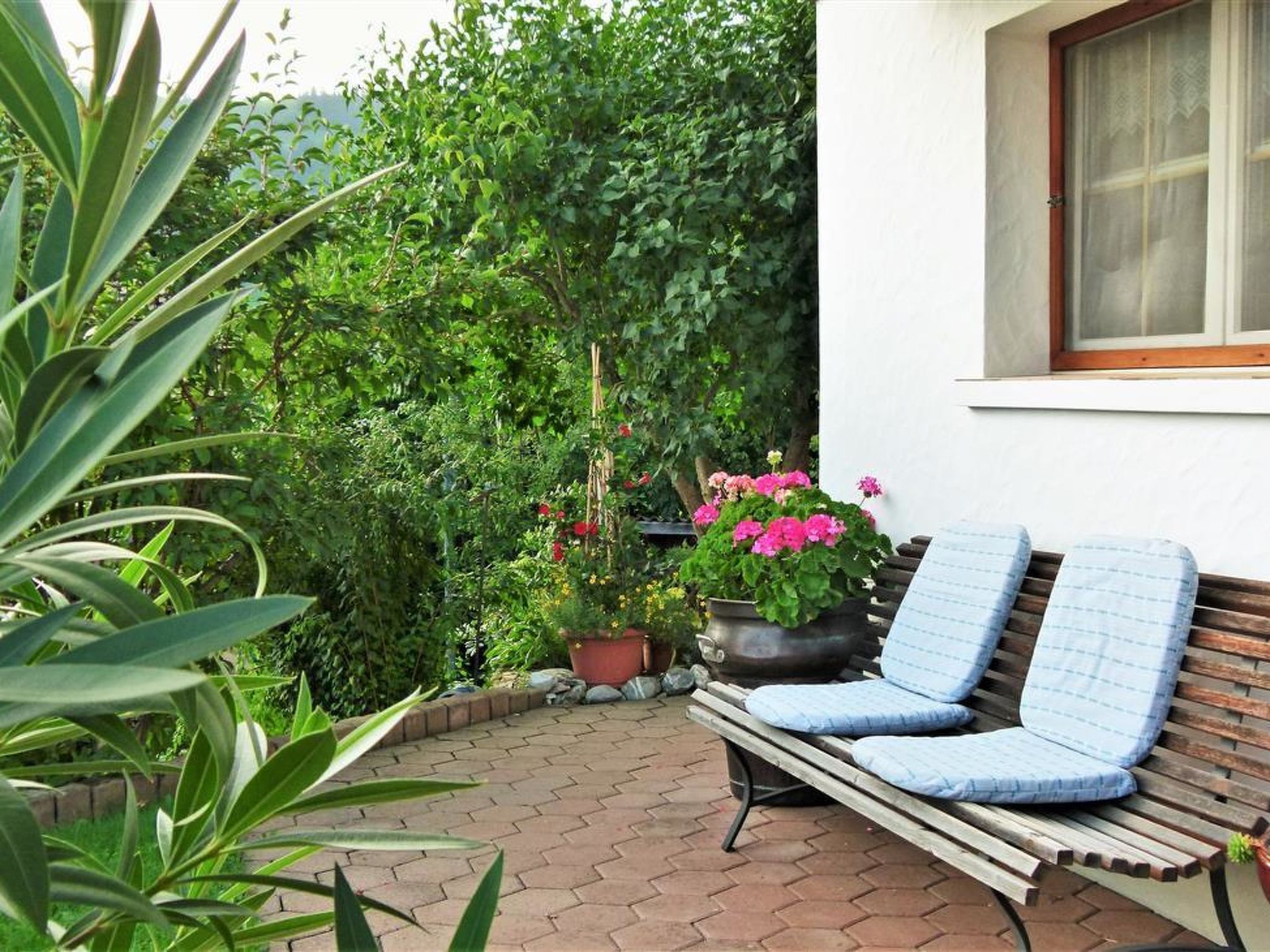 Eine Terrasse mit einer Holzbank, Topfpflanzen und einem Fenster.