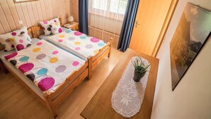 Une pièce chaleureuse avec deux lits en bois, une petite table ornée d’une plante et une fenêtre avec des rideaux.