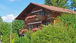 Un chalet en bois doté d’un toit à pente, de balcons ornés de jardinières et entouré d’une végétation luxuriante.