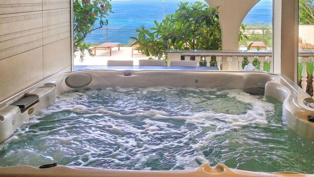 Un jacuzzi con vistas al mar y un balcón con mobiliario exterior.