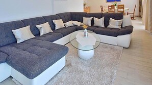 Una sala de estar moderna con un sofá modular gris, una mesa de centro de vidrio y un tapete blanco.