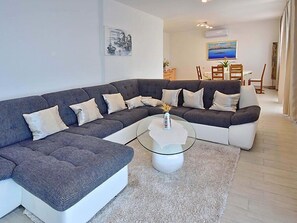 A modern living room with a grey sectional sofa, a glass coffee table, and a white rug.