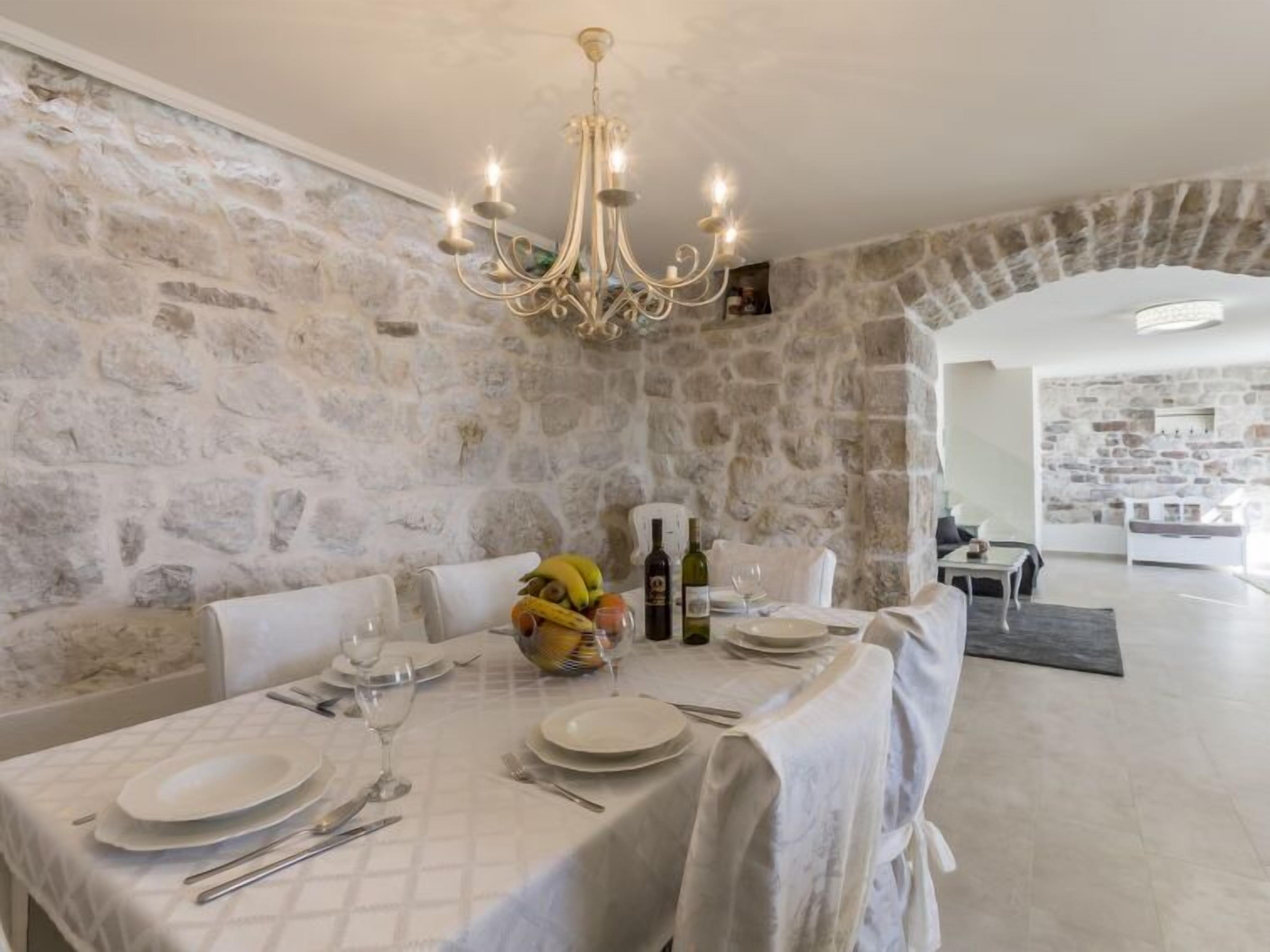 A dining area with a stone wall backdrop, a chandelier, and a table set for a meal.