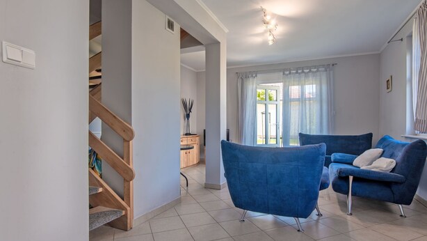 Ein modernes Wohnzimmer mit einer Treppe zu einer anderen Ebene, einer blauen Sofagarnitur und einem großen Fenster mit Vorhängen.