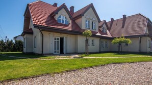 Ein zweistöckiges Haus mit rotem Ziegeldach, einem Hauseingang mit Tür und einem kleinen Baum im Vorgarten.