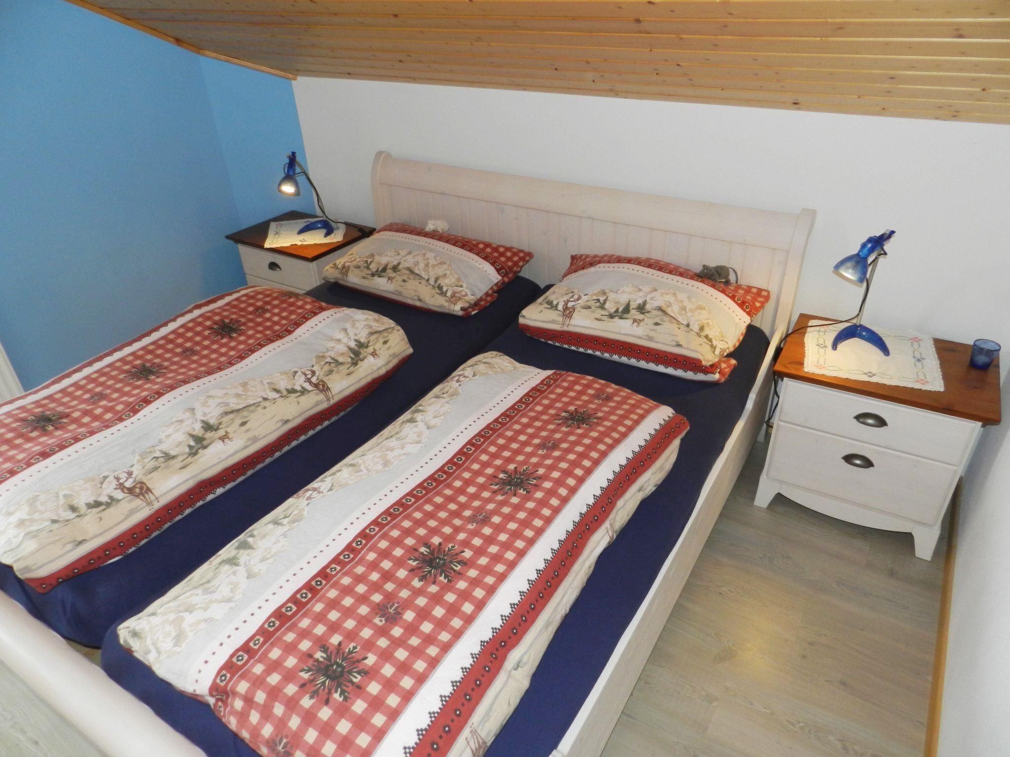A bedroom with two beds, each with a patterned bedspread and pillows, a bedside table with a lamp, and a nightstand with a lamp.