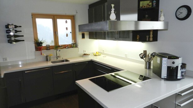 A modern kitchen with dark cabinets, a white countertop, a built-in oven, and a coffee machine. - Panorama, Chalet by Interhome (Zweisimmen)