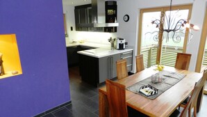 A modern kitchen with a built-in oven, a coffee machine, and a dining area with a wooden table and chairs. - Panorama, Chalet by Interhome (Zweisimmen)