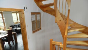 A wooden staircase leading to a second floor, a dining area with a table and chairs, and a view of a garden through a window. - Panorama, Chalet by Interhome (Zweisimmen)