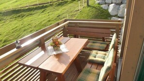 A wooden deck with a table and benches, overlooking a grassy area with rocks. - Panorama, Chalet by Interhome (Zweisimmen)