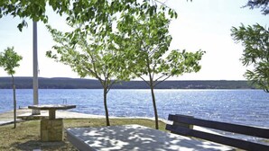 Un área de picnic junto al lago, con una mesa de piedra y bancos, rodeada de árboles y vistas al agua.