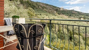 Un balcón con una silla y una mesa, con vista a una colina con edificios y árboles.