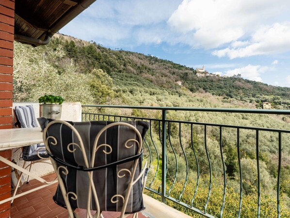 A balcony with a chair and table, overlooking a hillside with buildings and trees.