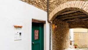 Un callejón estrecho con una puerta verde, un muro de piedra y un cartel que indica una habitación en alquiler.