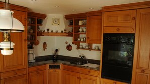 A kitchen with wooden cabinets, a black oven, and a clock on the wall. - Bärgchutzli Parterre by Interhome (Adelboden)