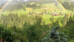A rural landscape with a rainbow arching over a village nestled in a valley surrounded by forests and mountains. - Bärgchutzli Parterre by Interhome (Adelboden)