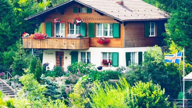 A two-story chalet with a balcony, surrounded by lush greenery. - Bärgchutzli Parterre by Interhome (Adelboden)