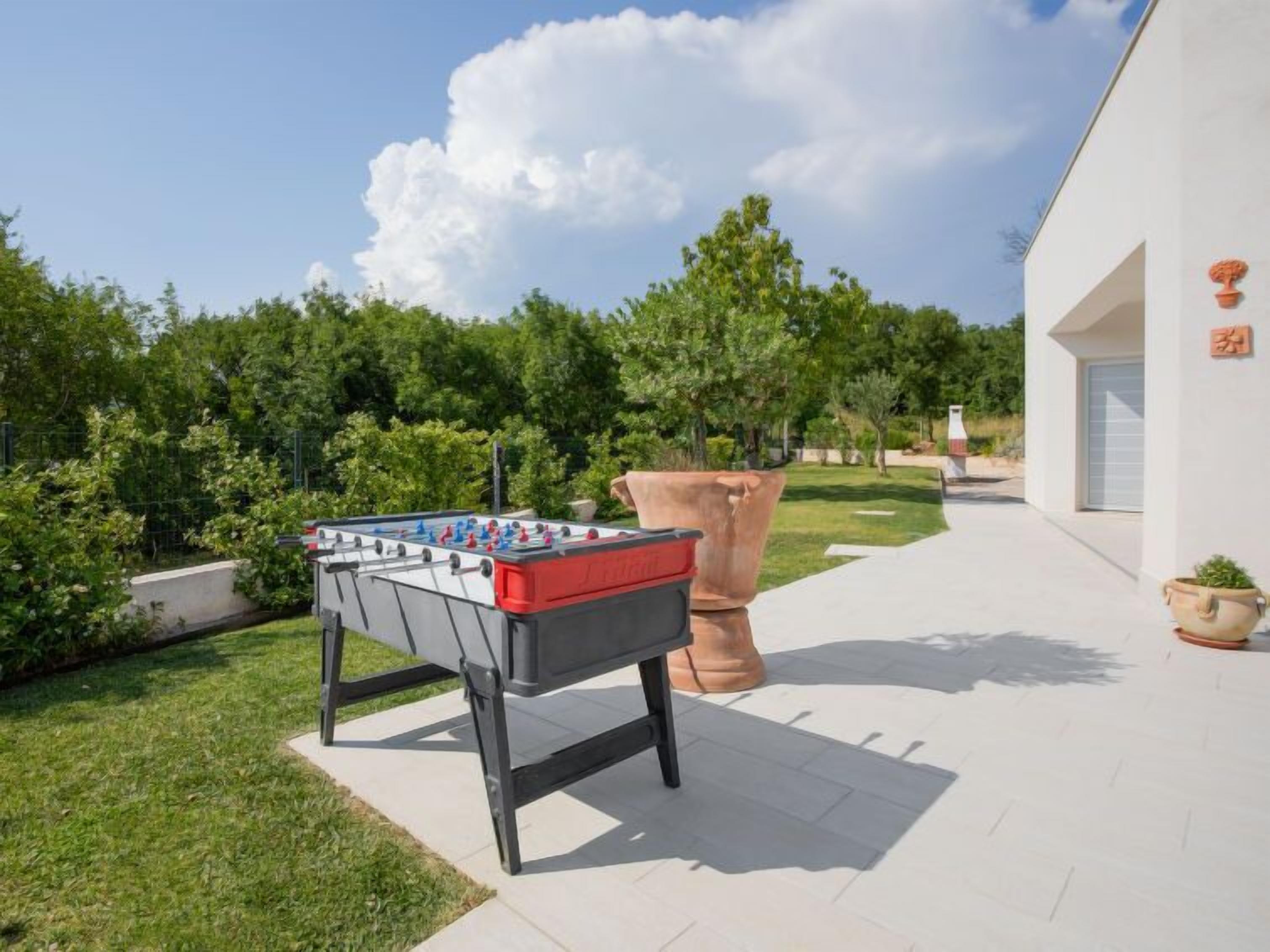An outdoor foosball table in a well-maintained garden area with a modern building in the background.