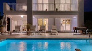 A two-story building with a swimming pool, outdoor seating, and a table with a foosball table.