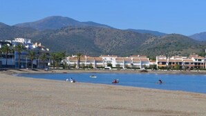 Un hotel frente al mar con varios edificios blancos, una playa de arena y montañas al fondo.
