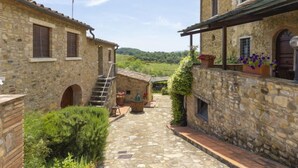 A stone building with a staircase leading to a second floor, a small outdoor seating area, and a view of a green landscape. - Le Buche by Interhome (Castellina in Chianti)